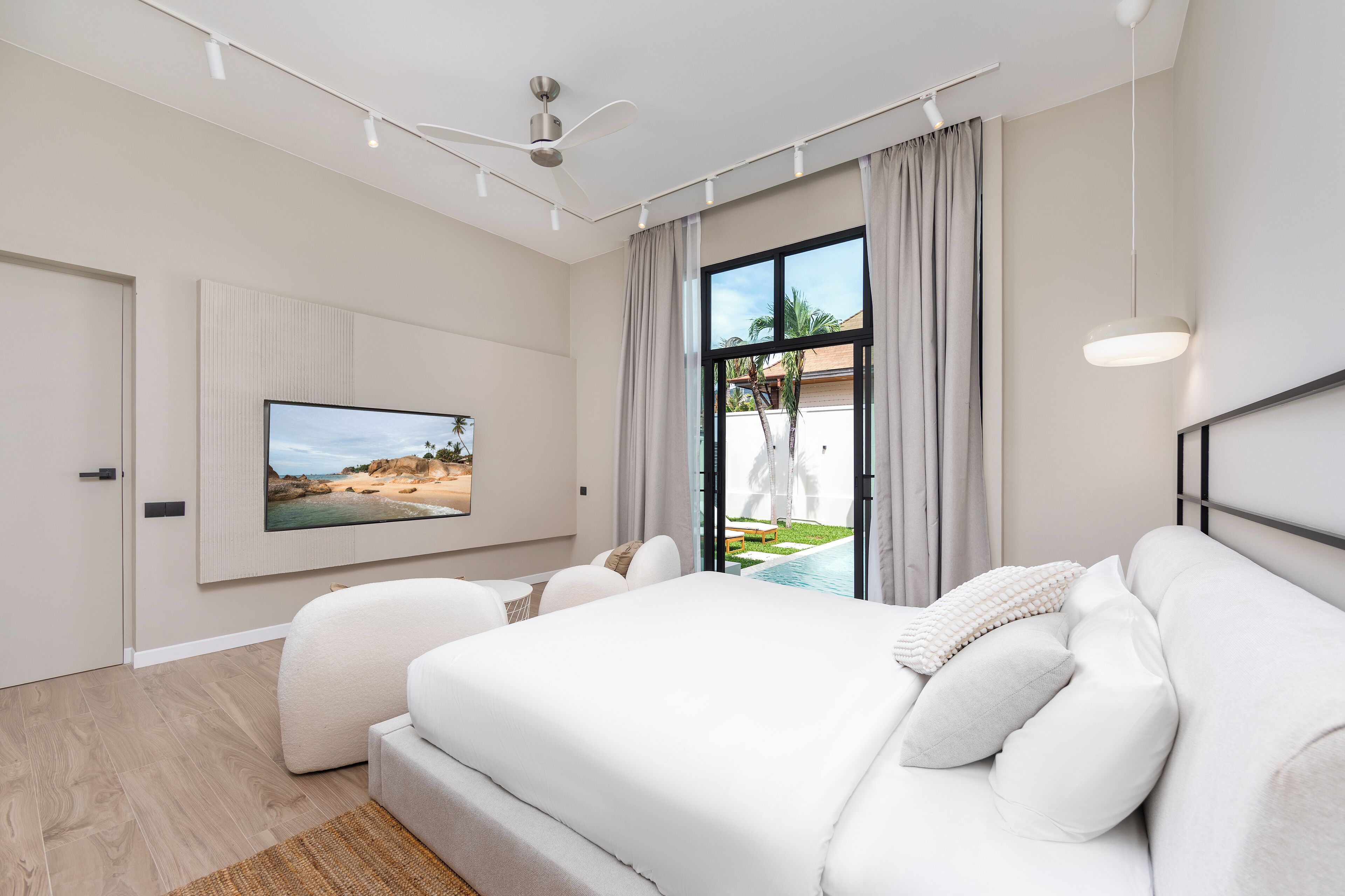 Ein modernes Schlafzimmer mit einem großen Bett, einem an der Wand montierten Fernseher und Blick auf einen Swimmingpool.