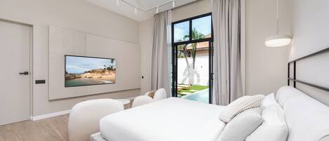 Ein modernes Schlafzimmer mit einem großen Bett, einem an der Wand montierten Fernseher und Blick auf einen Swimmingpool.