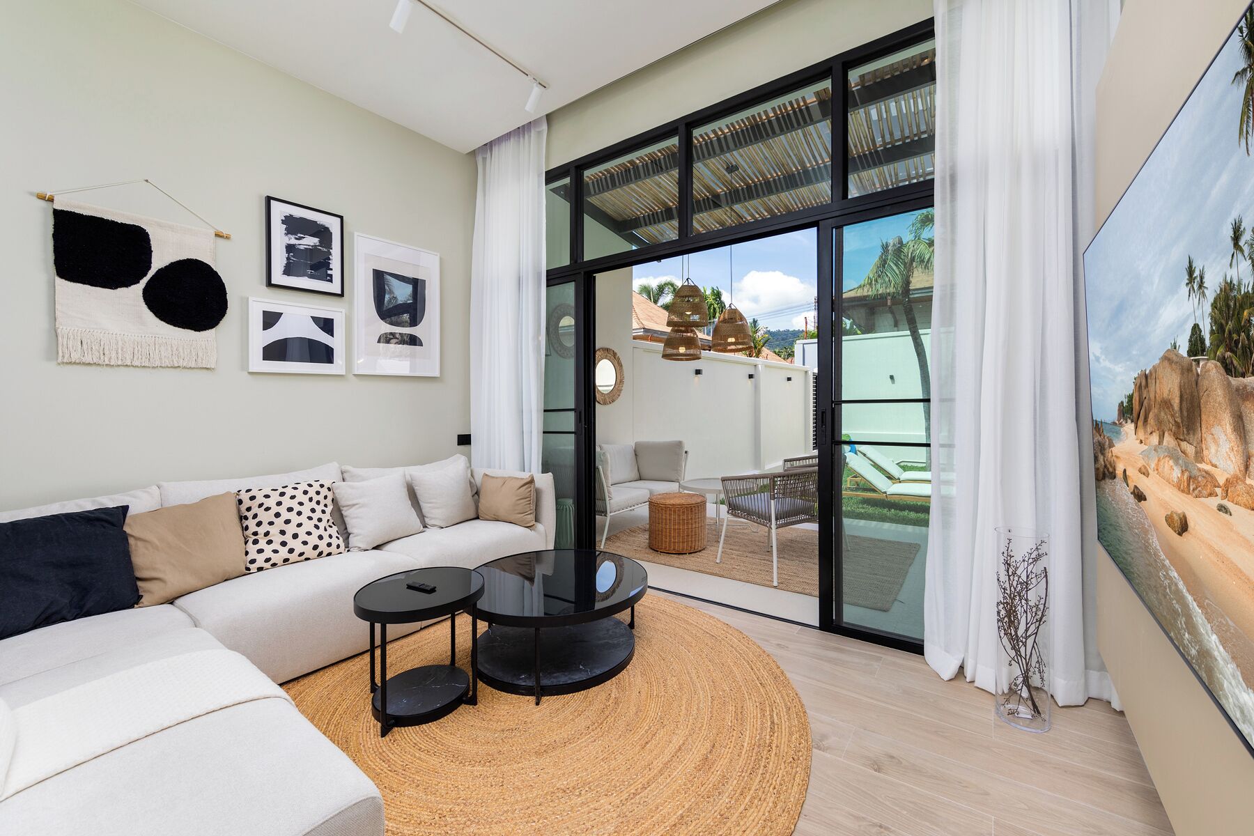 A modern living room with a sofa, two side tables, and a large glass door leading to an outdoor area with a view of the beach.