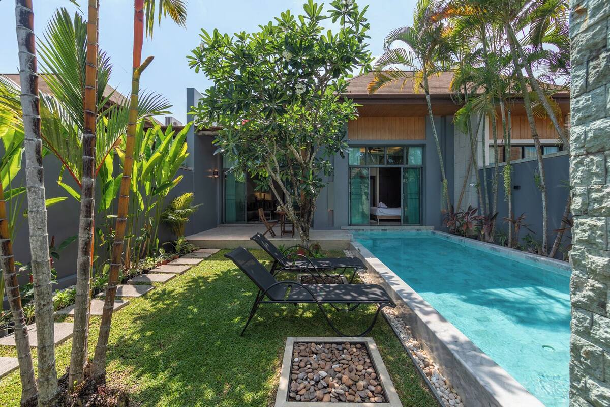 A modern house with a swimming pool, a covered patio, and a garden with tropical plants.
