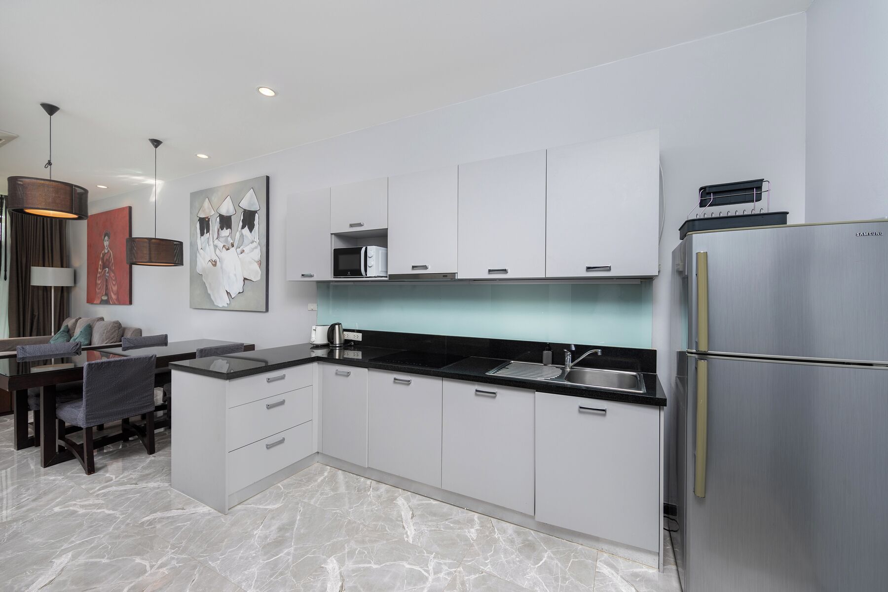 Een moderne keuken met witte kastjes, een roestvrijstalen koelkast en een eethoek met een tafel en stoelen.