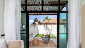 A modern living room with a sofa, a coffee table, and a view of a patio with outdoor furniture and a pool. - Onyx Villas by TropicLook (Rawai)