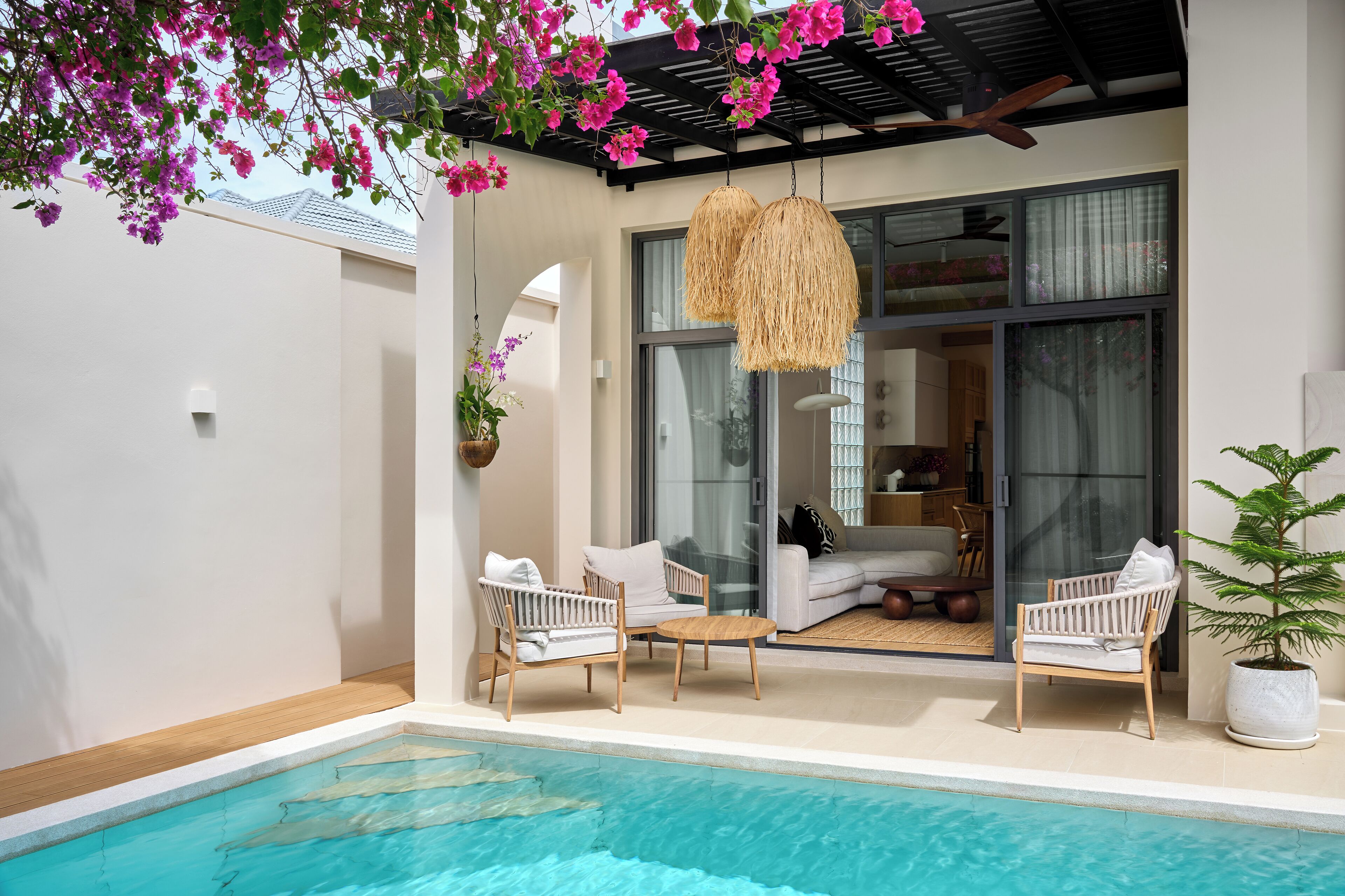 A poolside area with white wicker chairs and a hanging wicker lamp.