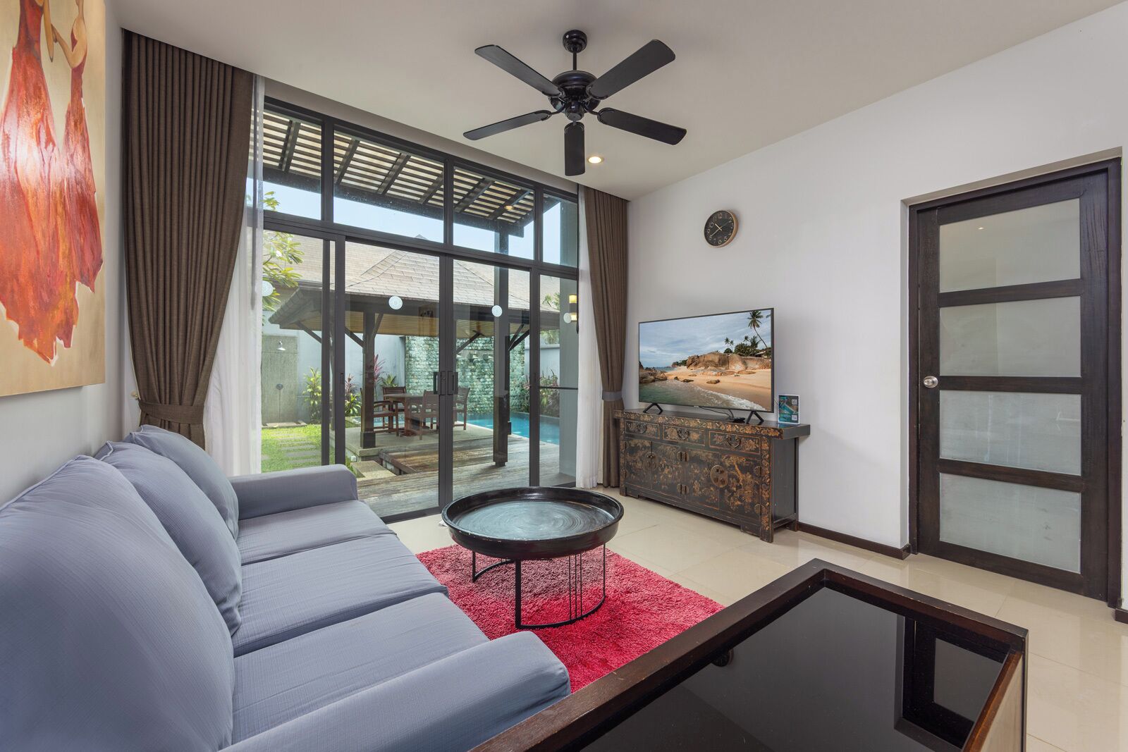 A living room with a sofa, a coffee table, a TV, and a view of a swimming pool.