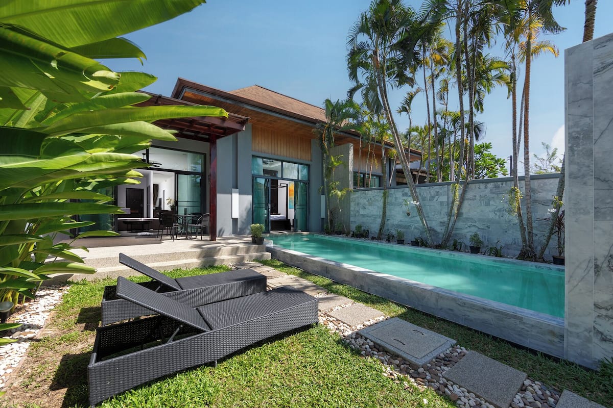 A modern house with a swimming pool, outdoor seating, and tropical plants.