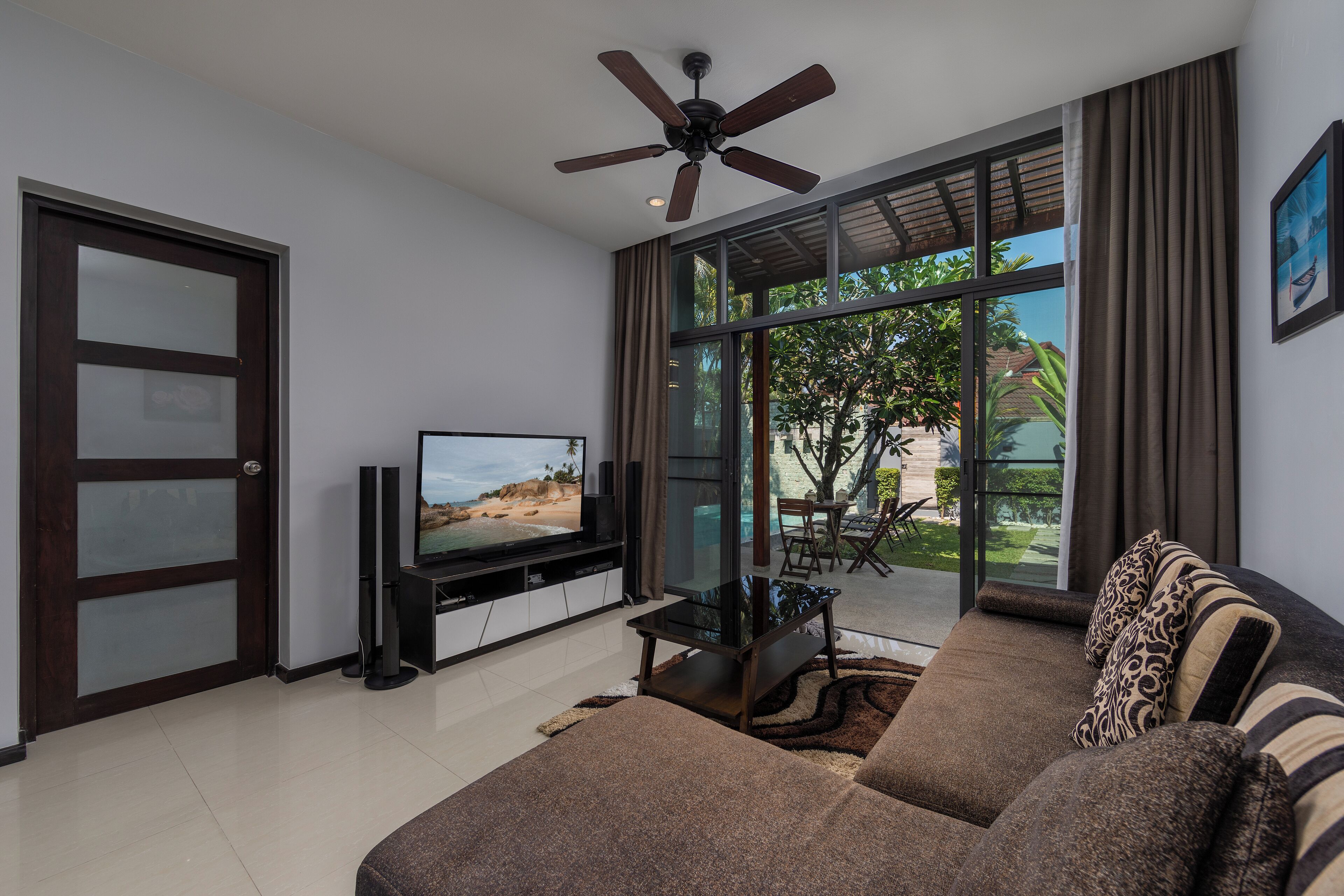A modern living room with a large TV, a sofa, and a ceiling fan.