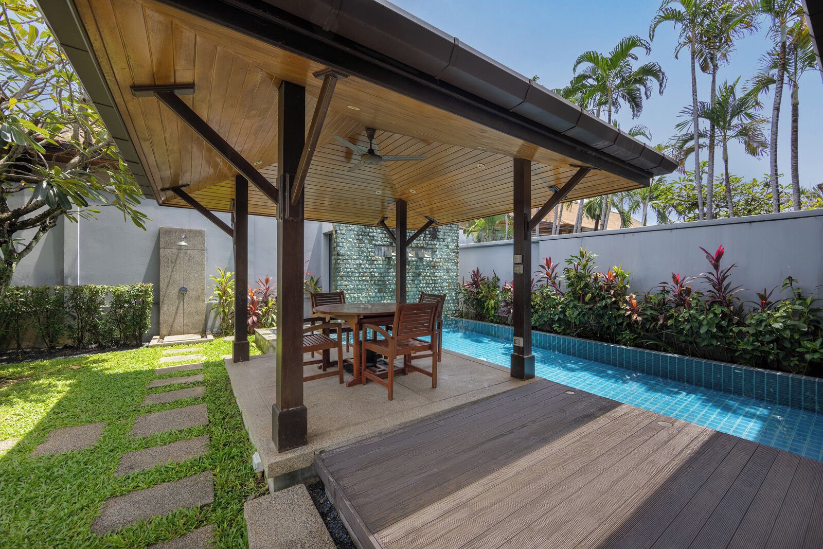 A covered outdoor area with a pool, wooden furniture, and a stone pathway.