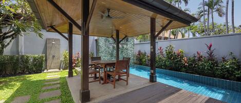 A covered outdoor area with a pool, wooden furniture, and a stone pathway.