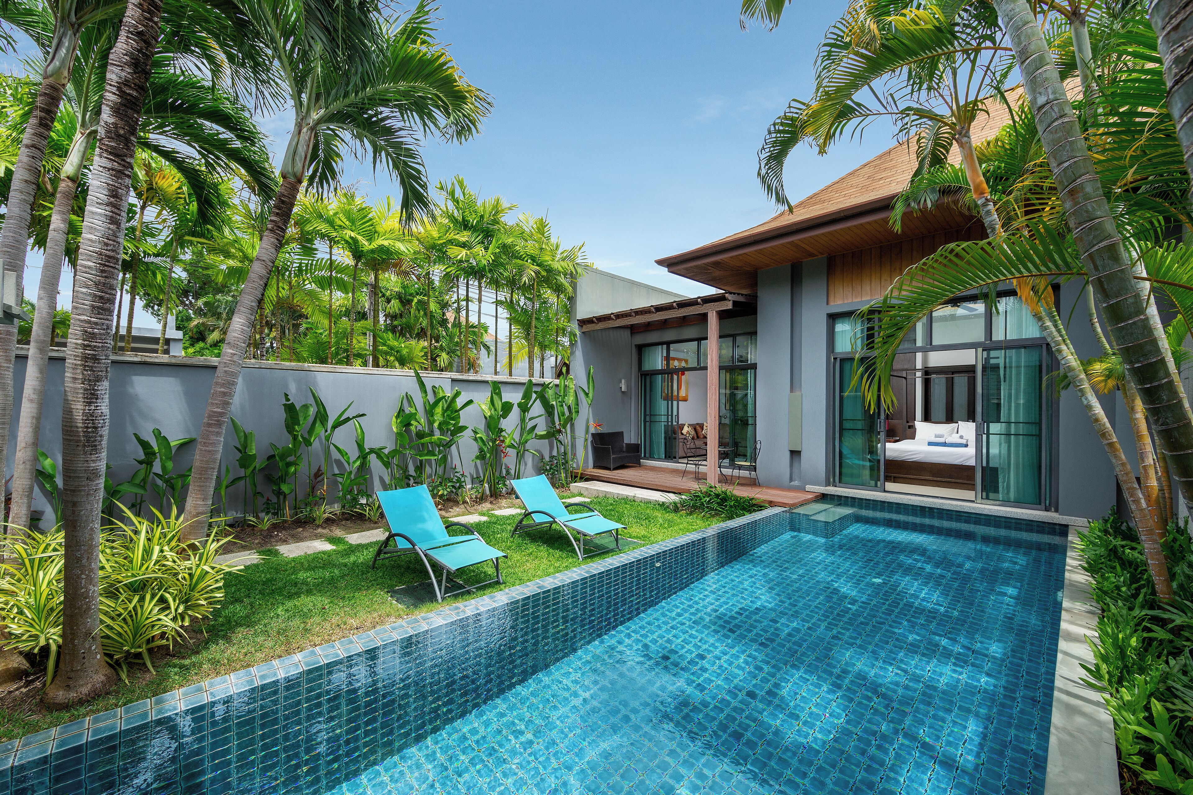 A modern pool area with a clear blue pool, two lounge chairs, and lush tropical plants.