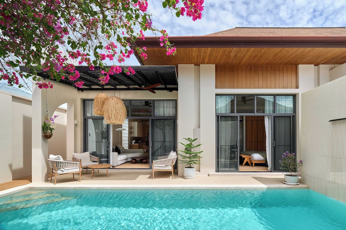 A modern outdoor pool area with a wooden ceiling, two hanging wicker lamps, and a seating area with a sofa and chairs.