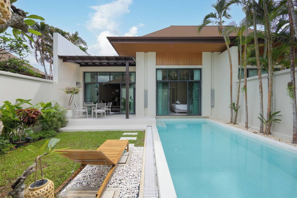 A modern house with a swimming pool, a covered patio, and a garden with tropical plants.