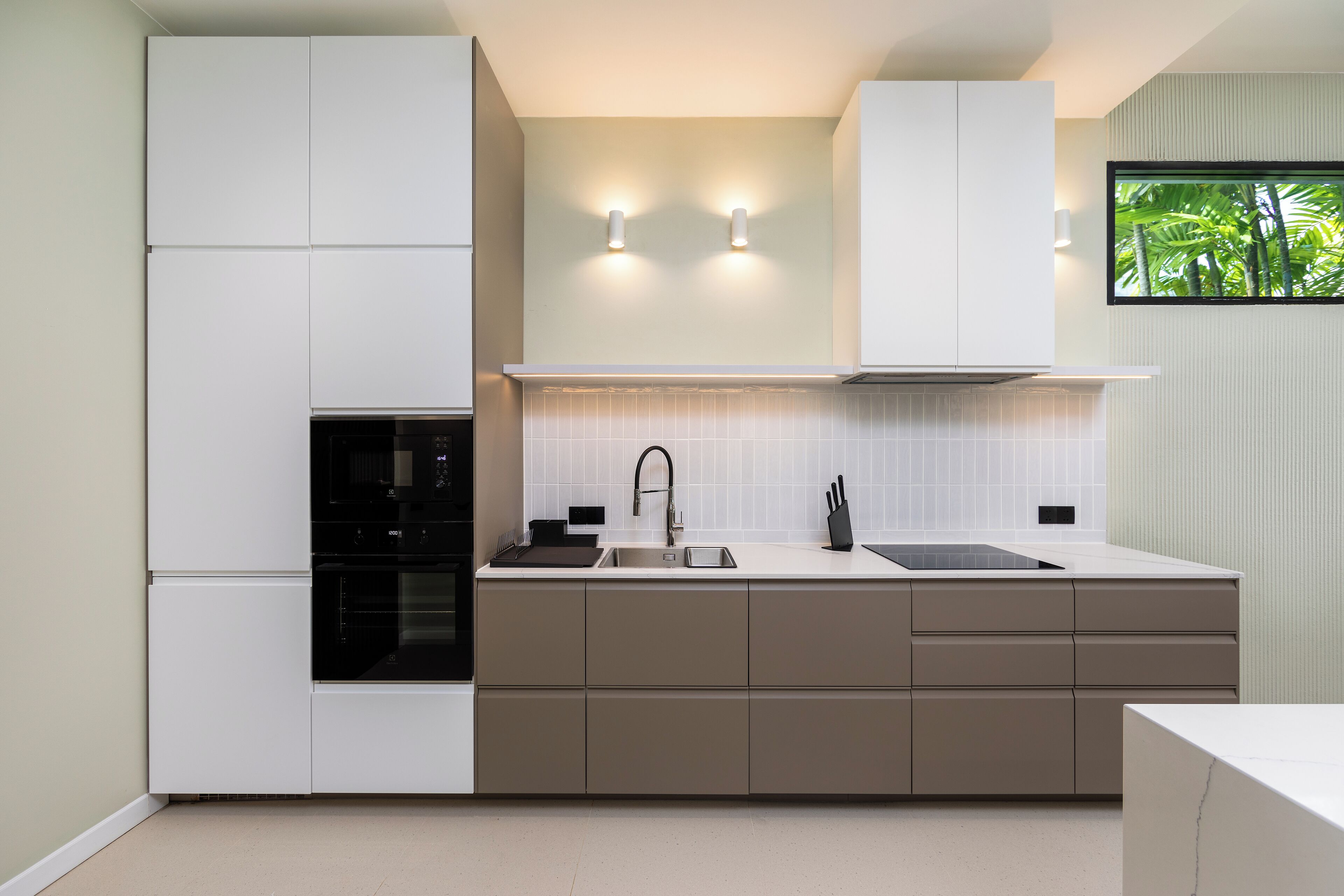 A modern kitchen with white cabinets, a black oven, a stainless steel sink, and two wall-mounted lights.