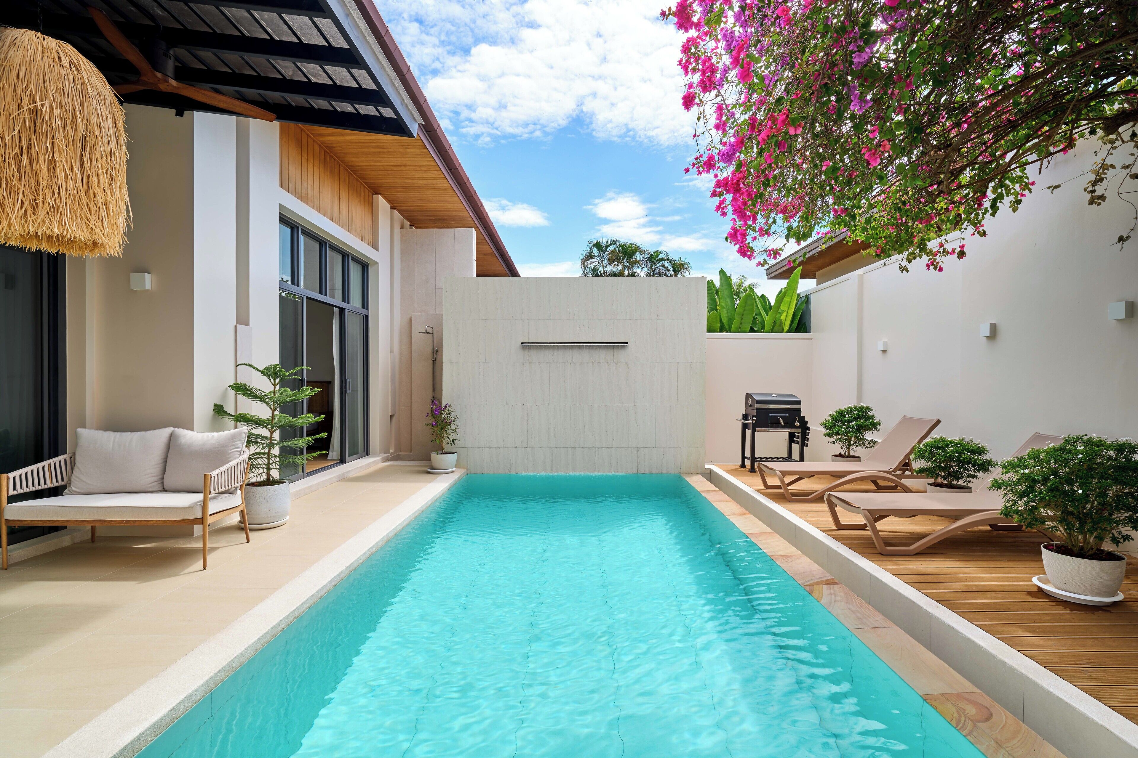 Ein Swimmingpool mit Liegestühlen und einer Sitzecke, umgeben von Topfpflanzen und einer Pergola mit blühendem Efeu.