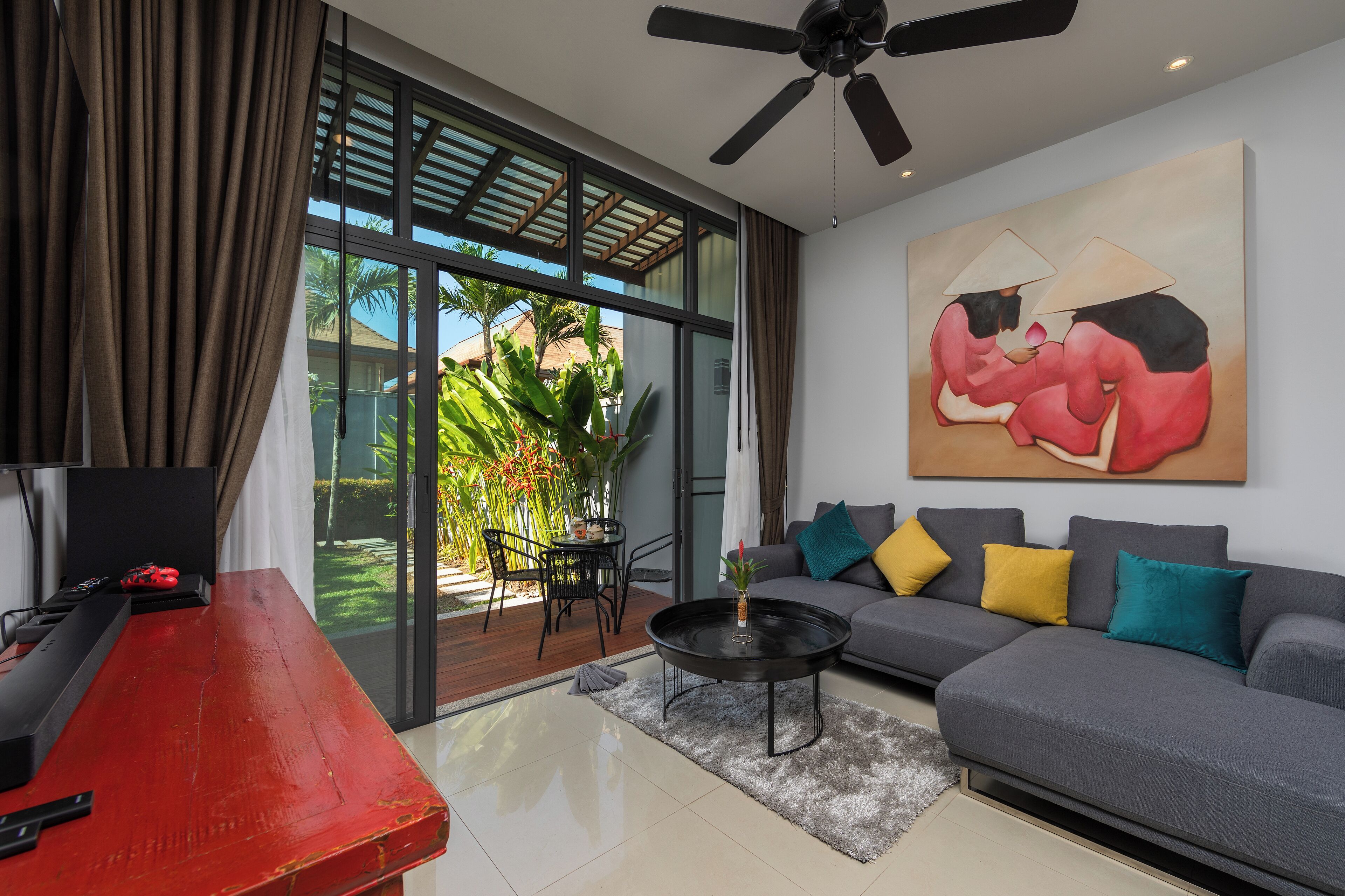 A modern living room with a grey sofa, a red table, and a ceiling fan.