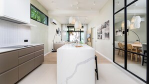 Et moderne køkken med en central ø, et spiseområde med bord og stole, og et stort vindue der giver naturligt lys.