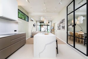 A modern kitchen with a central island, a dining area with a table and chairs, and a large window providing natural light.