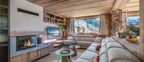 A modern living room with a fireplace, wooden ceiling, and large windows.