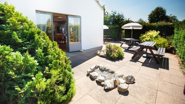 A modern outdoor patio with a fire pit, picnic tables, and a glass door leading to a room. - The Raceby Hotel, Doncaster (South Yorkshire), Part of the AG Collection (Doncaster)