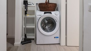 Un lavadero pequeño con una lavadora de carga frontal, una cesta encima y un aspirador a la izquierda.