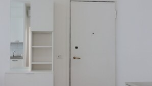 Una puerta blanca con pomo de latón, un mueble blanco con espejo y repisa, y una encimera blanca con lavabo.