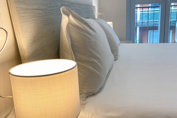 A bed with a white headboard and pillows, a bedside lamp, and a window with a view of buildings.