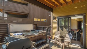 An outdoor hot tub area with a wooden deck, two Adirondack chairs, and a glass door leading to a patio. - New! Hot Tub, Soaking Tub, Great Location! (Big Sky)