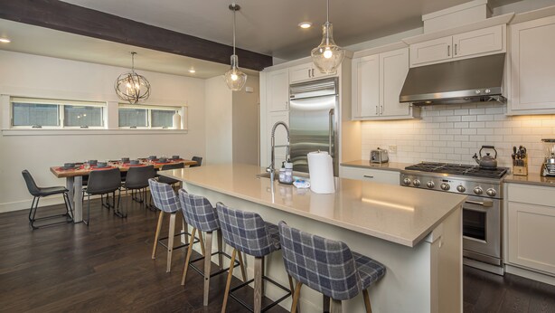 A modern kitchen with a central island, bar stools, a stainless steel refrigerator, and a gas stove. - New! Hot Tub, Soaking Tub, Great Location! (Big Sky)
