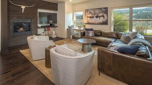A modern living room with a fireplace, leather sofas, and a large window offering a view of the outdoors. - New! Hot Tub, Soaking Tub, Great Location! (Big Sky)