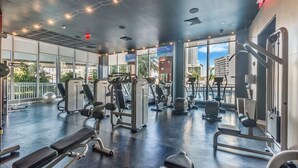 A gym with various exercise equipment, large windows, and a view of the city. - Studio with Garden View and Balcony – 3rd Floor (Hallandale Beach)