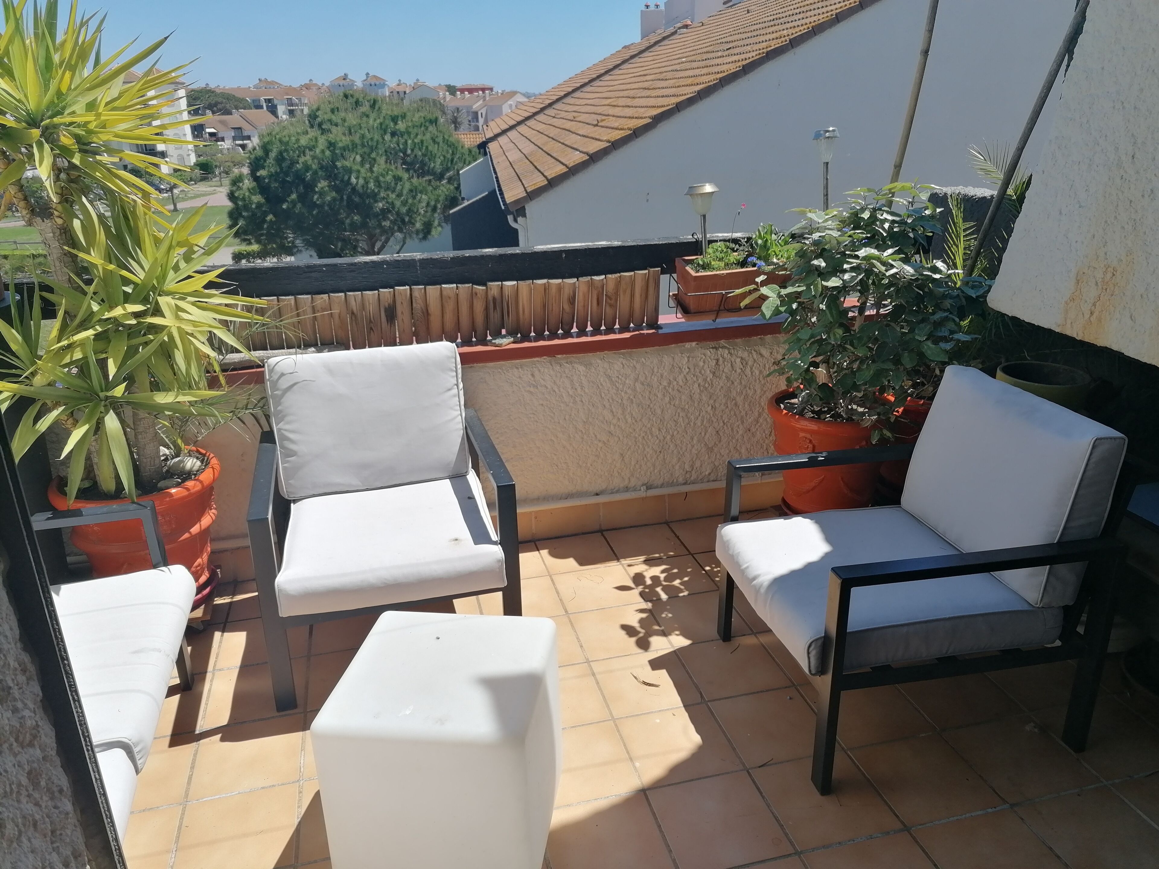 Eine Terrasse mit zwei weißen Stühlen und einem kleinen Tisch, umgeben von Topfpflanzen.