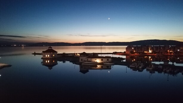 A calm waterfront with buildings reflecting on the water, a crescent moon in the sky, and distant mountains. - Air-conditioned apartment with splendid panoramic view - COUDALERE pedestrian village (barcares)