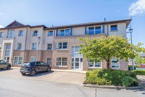 A multi-story building with a parking lot, a tree, and a sign indicating 'Riverside Garden.' - Stylish 2-BR Apt | Parking & Wi-Fi | Sleeps 4 (Highland Council)
