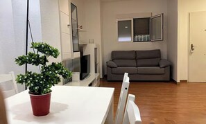 Een woonkamer met een grijze bank, een witte tafel met een rode pot en een televisie.