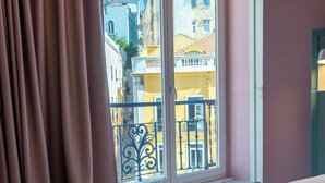 A hotel room with a bed, a window with curtains, and a view of buildings outside. - Boavista 83 Hostel Lisbon (Lisbon)