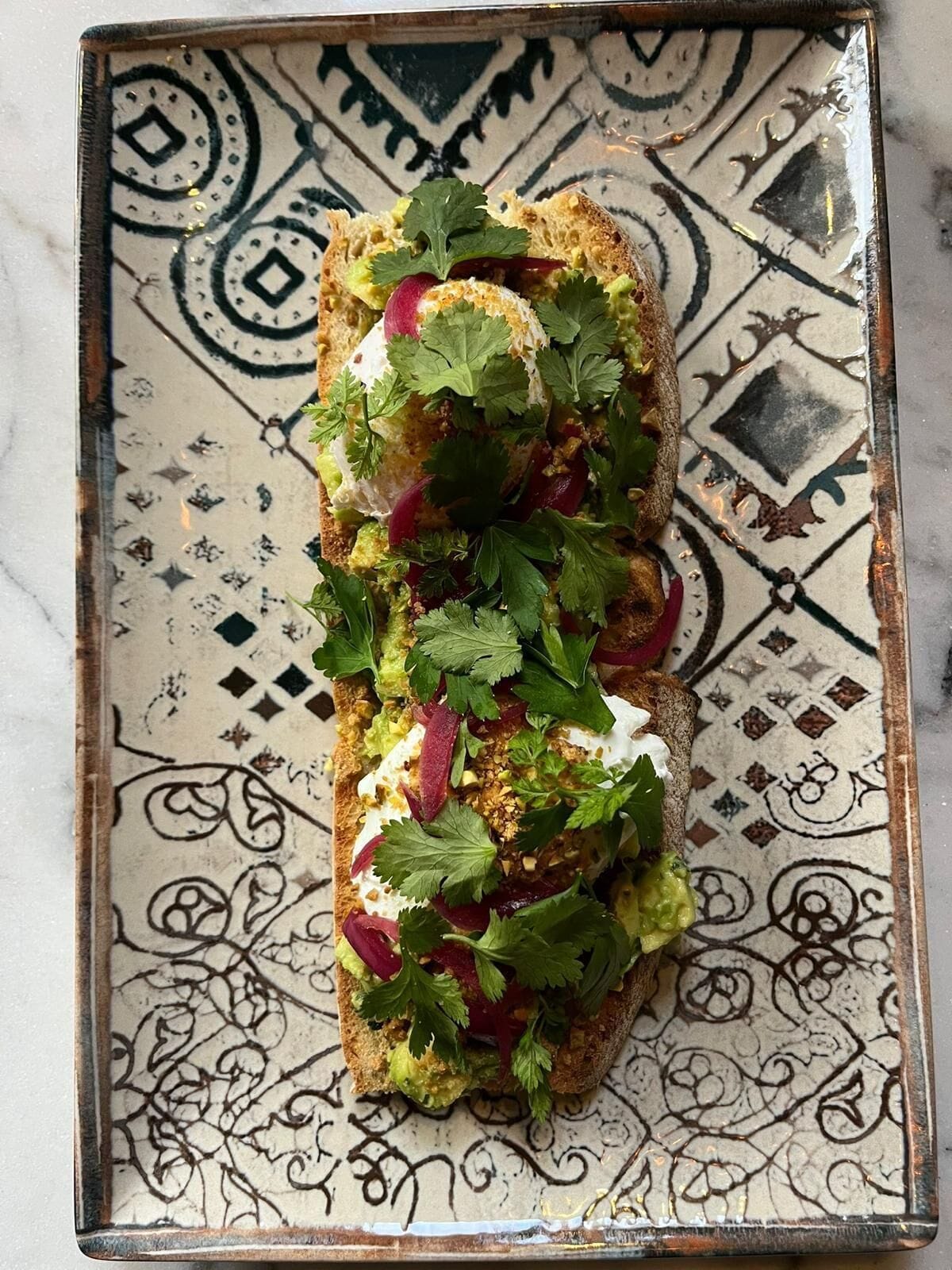 Un plato rectangular con diseño estampado, que contiene un sándwich de aguacate, rábano y cilantro.