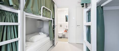 Una habitación compacta y bien iluminada con literas, un baño pequeño y una puerta que da a otra habitación.