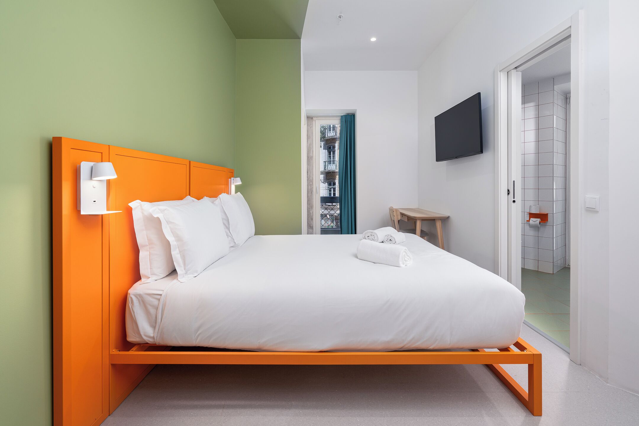 Un dormitorio moderno con una cama, un televisor y un baño visible a través de una puerta abierta.