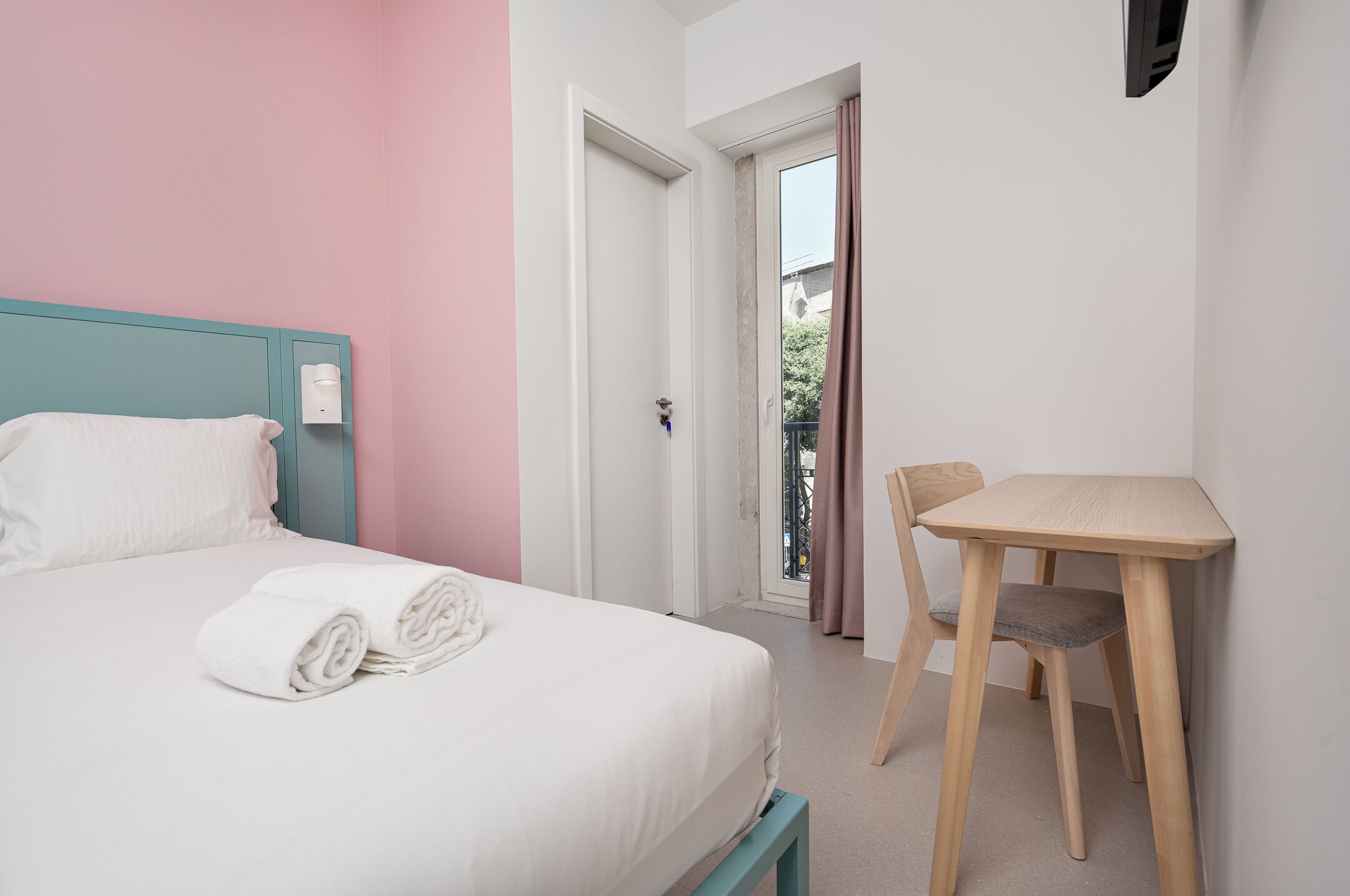 A bedroom with a bed, a chair, a desk, and a door leading to a balcony.