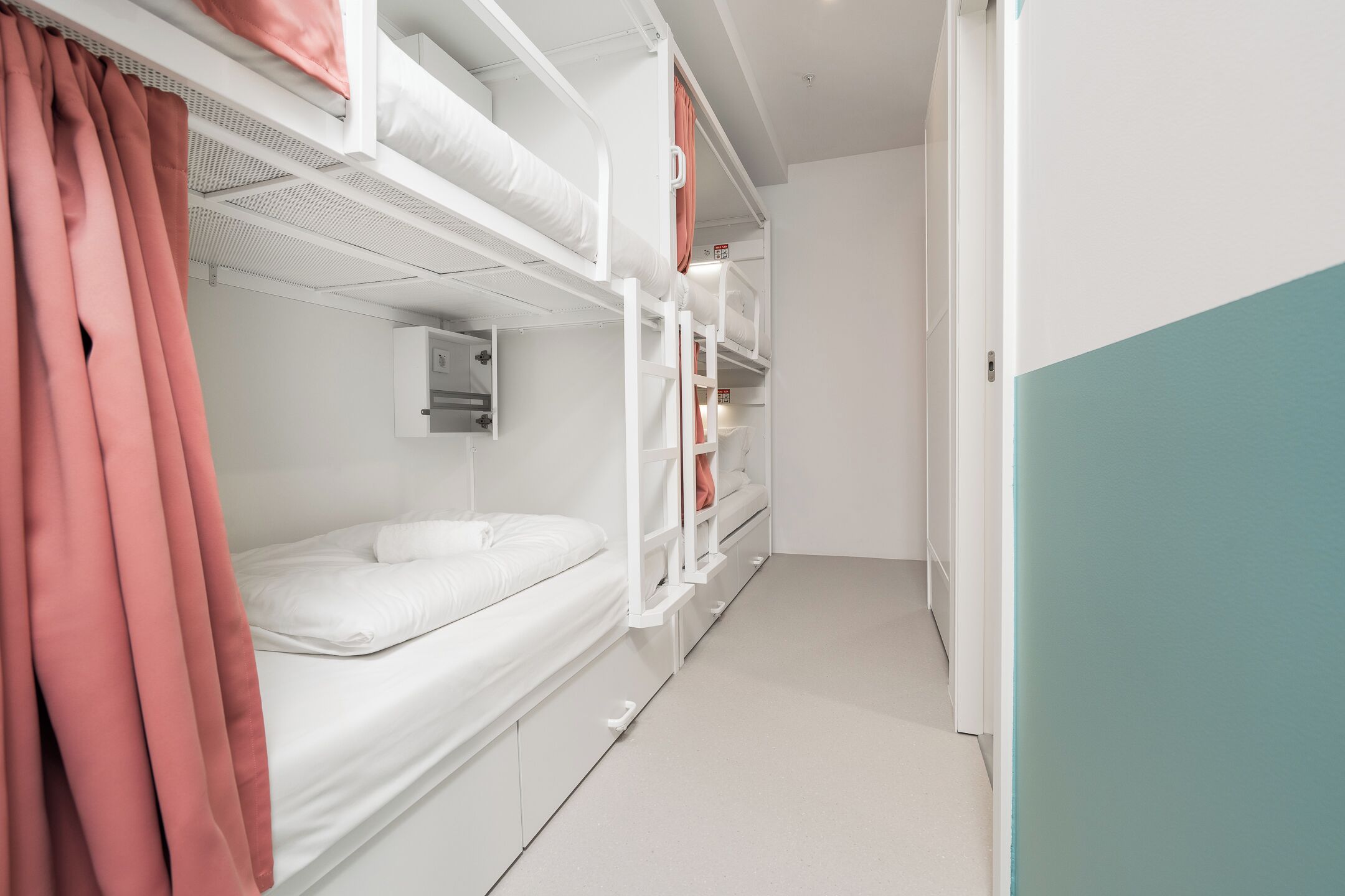 Quarto com beliche, colchão branco, cortina rosa e armário branco.