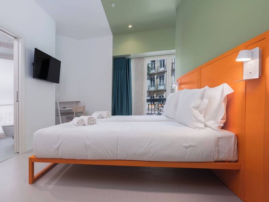 Una camera d'albergo moderna con un letto, una televisione e vista sugli edifici dalla finestra.