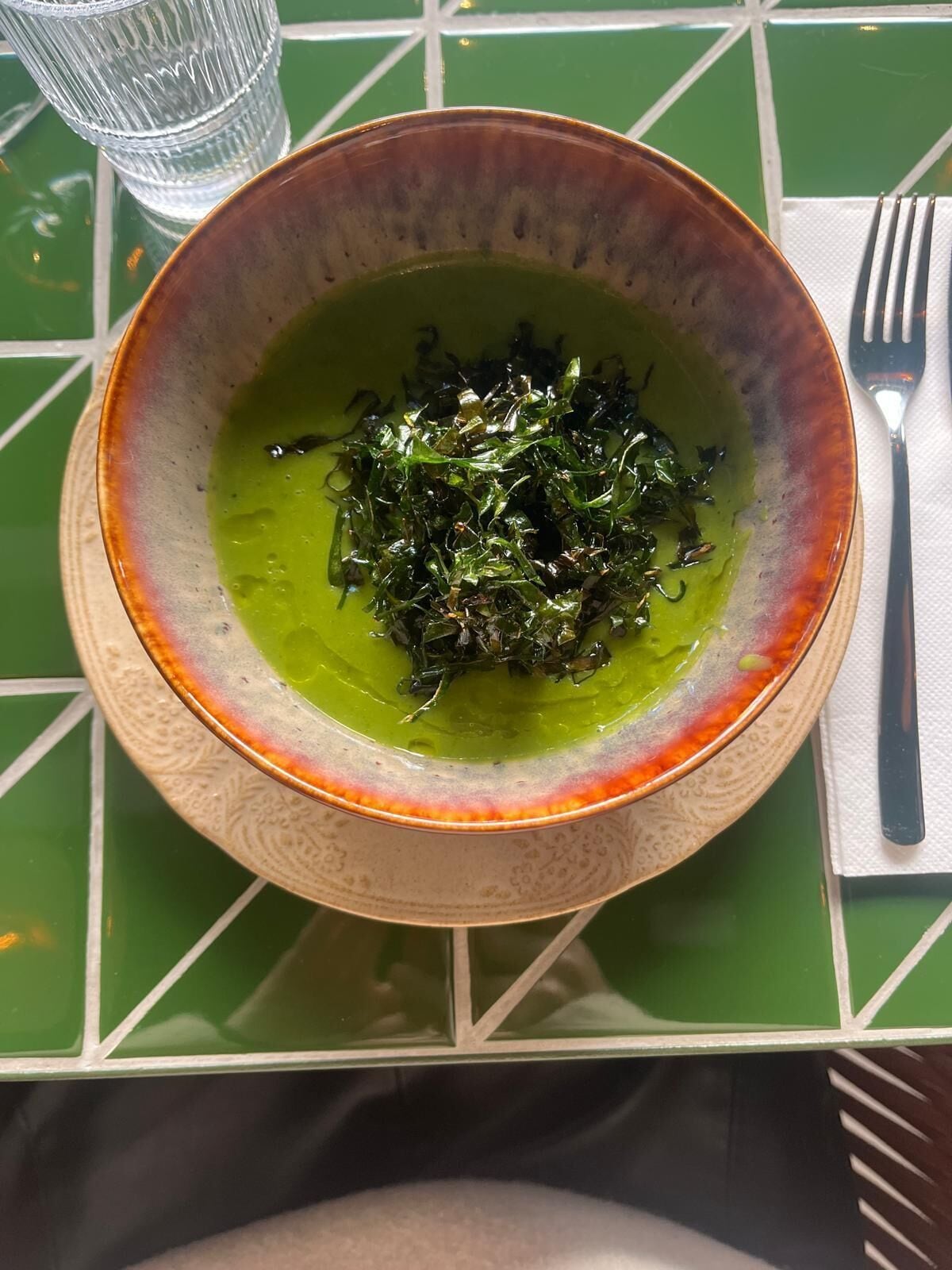 A bowl of green soup with seaweed on a table with a green and white checkered tablecloth.