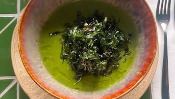 A bowl of green soup with seaweed on a table with a green and white checkered tablecloth.