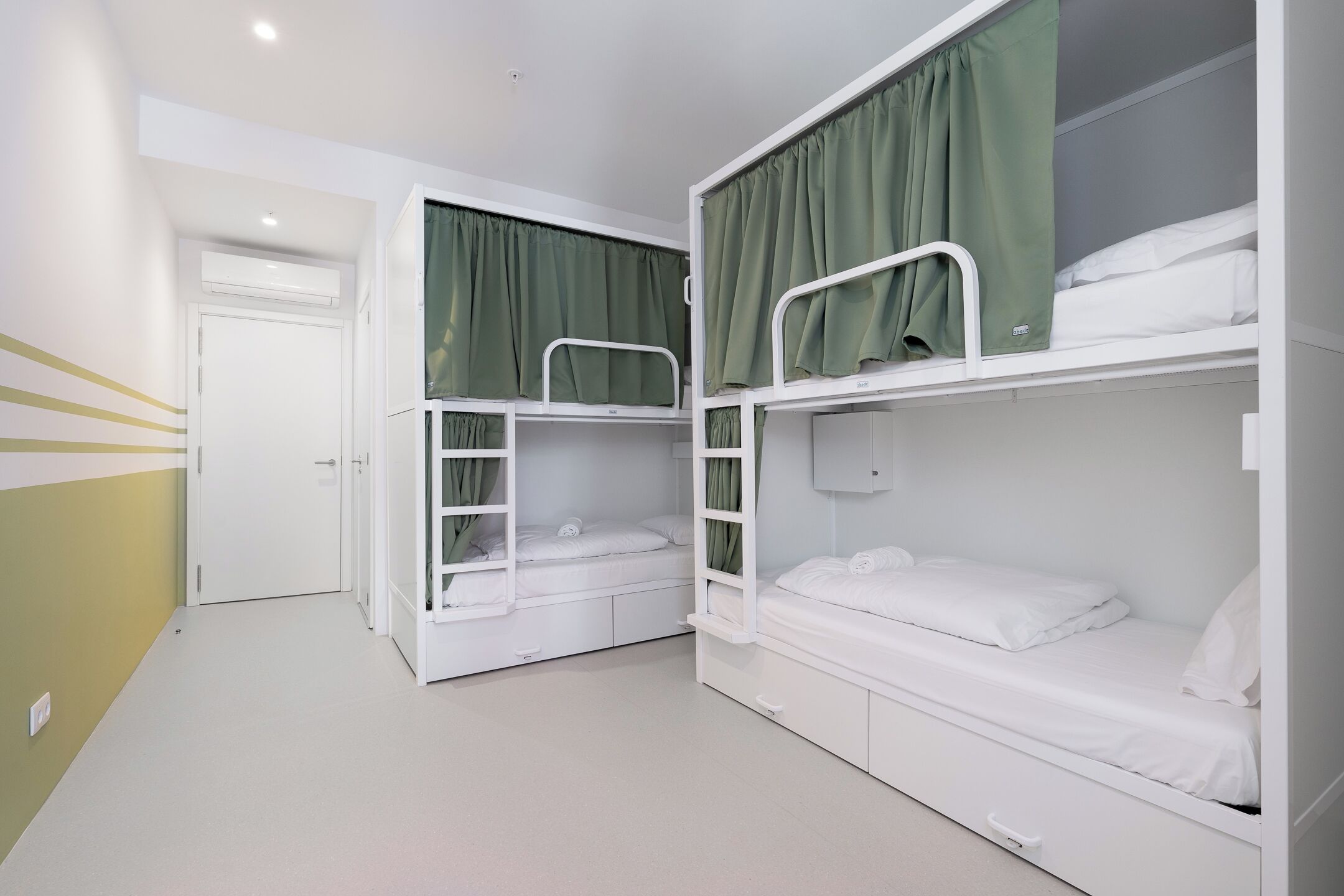 Una habitación con literas, una puerta blanca y una cortina verde.