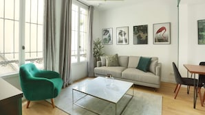 A modern living room with a sofa, a green armchair, a dining table, and artwork on the wall.