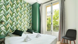 A hotel room with a bed, a chair, a window with curtains, and a green wall with a leaf pattern.
