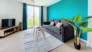 Un salon moderne avec un mur d’accent de couleur turquoise, un canapé gris, un téléviseur posé sur un meuble en bois et une grande plante en pot.