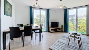 Un salon moderne avec un coin repas, de grandes fenêtres et un téléviseur posé sur un meuble en bois.