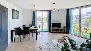 Un salon moderne avec un coin repas, de grandes fenêtres et un téléviseur.