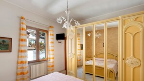 A bedroom with a bed, a wardrobe with a mirror, a chandelier, and a window with curtains.