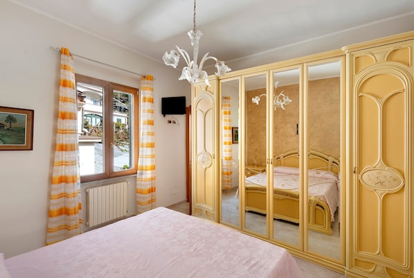 A bedroom with a bed, a wardrobe with a mirror, a chandelier, and a window with curtains.